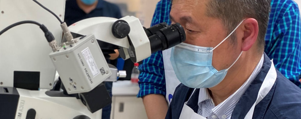 A man looking into a microscope, wearing a respiratory mask.